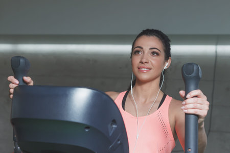 Sporty young woman makes sport exercises on the electrical trainer in the gym, soft focus background