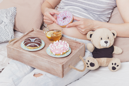 Pregnant woman with different colored donuts and a cup of tea, soft focus backgroundの写真素材