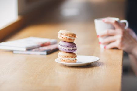 Hands with a cup of coffee and macarons, soft focus backgroundの写真素材