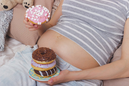 Pregnant woman with different donuts on the plate, soft focus background
