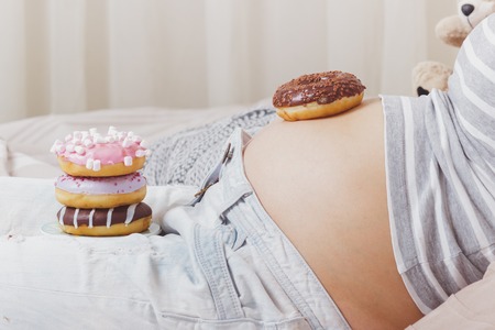 Pregnant woman with different donuts on the plate, soft focus backgroundの写真素材