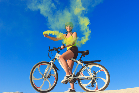 Young woman on the top of the mountain holds a yellow signal smoke in her handの写真素材