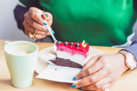 Young dark-skinned woman dressed in casual clothes holding cup of hot drink, enjoying coffee or tea. Black student girl spending morning at cafeの写真素材