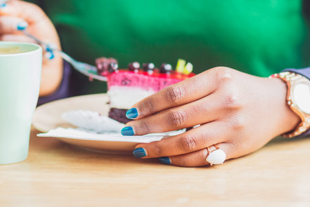 Young dark-skinned woman dressed in casual clothes holding cup of hot drink, enjoying coffee or tea. Black student girl spending morning at cafeの写真素材