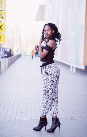 Young dark-skinned woman dressed in fashion clothes walking on the street, blurred backgroundの写真素材
