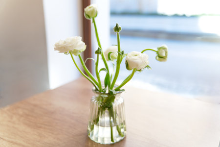 White flowers in glass vase on wooden table in the room.の写真素材