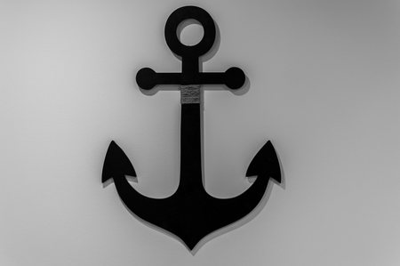 Black anchor hanging on a white wallの写真素材