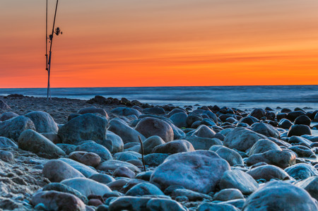 Sunset over the sea. Stones and fishing rods on the foregroundの写真素材