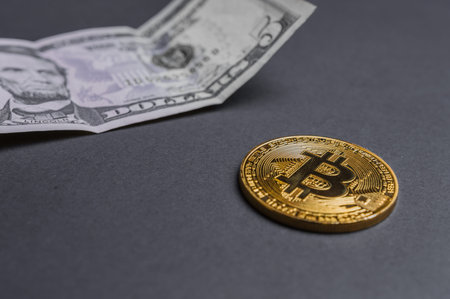 Bitcoin on black background with dollar bill in the back