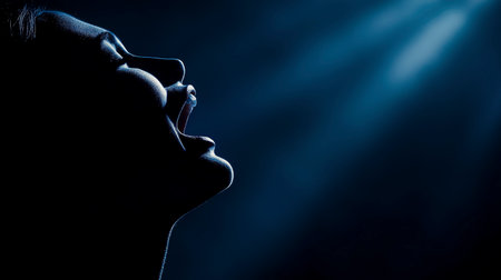 Silhouette of a young woman singing in the dark, close upの写真素材