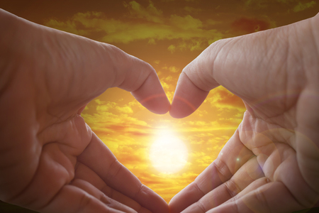 Hands made heart shape with sunlight and sky backgroundの写真素材