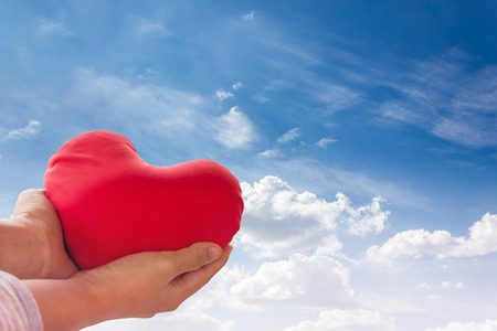 Romantic lovely valentine concept with hand gently raise up red heart on blue sky backgroundの写真素材