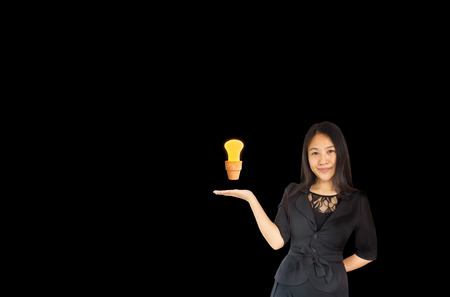 (With clipping path) Smiling business women Asia women presenting  light bulb in small flower pot on black backgroundの写真素材