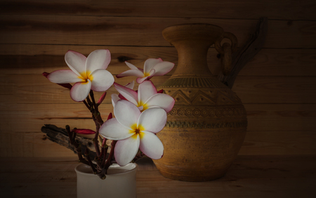 (Soft sepia and antique colour tone) Sweet pink yellow white flower plumeria or frangipani bunch with old vintage baked clay vase and wood backgroundの写真素材