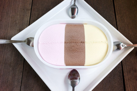 Top view icecream vanilla,strawberry and chocolate flavour on white plate with spoons on wood tableの写真素材