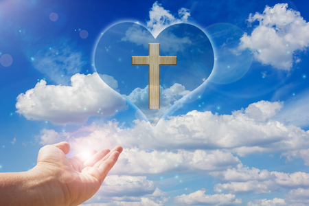 Crucifix and light on heart background  with handの写真素材