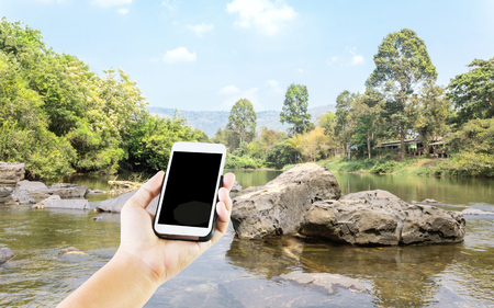 Lady hand presenting or show blank screen mobile phone on river, mountain and tree backgroundの写真素材