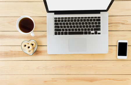 Top view blank or empty screen notebook computer or laptop with cup of black coffee and cookie with smartphone on jointed wooden table for technology concept backgroundの写真素材