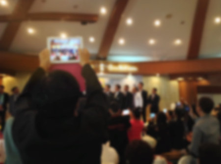 Blurred background of man recording video or taking picture by smartphone at stage in meeting room, crowd in hallの写真素材