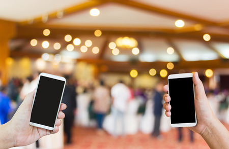 Hand show or present big blank screen mobile or cellphone or smartphone on blurred event hall,transfering data or business cantact,business to business の写真素材