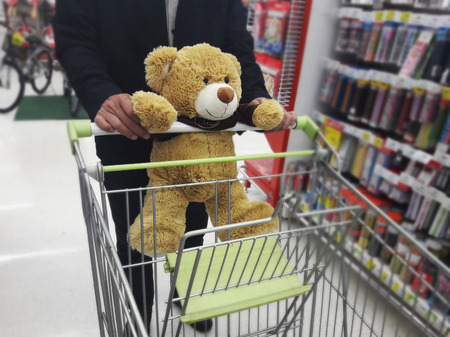 Cute brown bear catching shopping cart with man with background of departmentstoreの写真素材