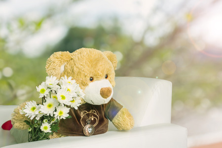 Cute brown bear doll with white flower bouquet in romantic green bokeh, bear gift and heart necklace, romantic in love bearの写真素材