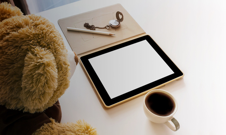 Cute bear doll watching blank screen laptop to smartphone or tablet on work table with cup of hot coffeeの写真素材