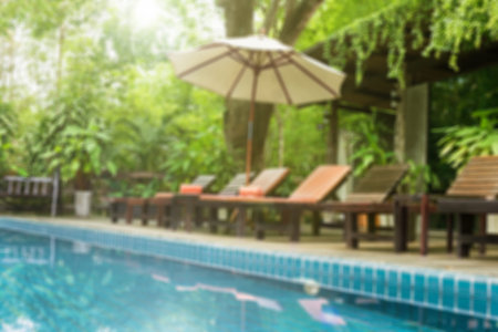 Blurred background view of summer mood, big umbrella and pool chair beside swimming pool
