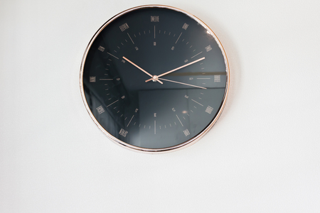 Modern black clock hanging on plain wallの写真素材