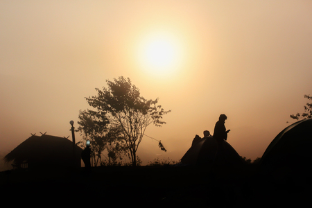 Silhouette dark man, hut and tree shadow in densely fog in winter morning with sunrise background on skyの写真素材