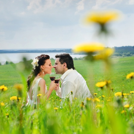 Bride and Groom kissing with a glasses in the field of dandelionの写真素材