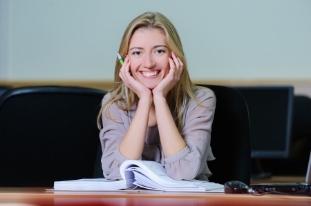 Smiling young girl in the office sitting at a table with a pen and bookの写真素材
