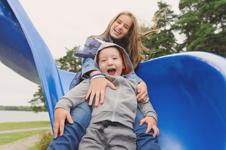 Smiling girl and boy having fun on childrens slideの写真素材