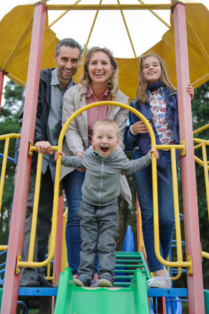 Positive parents with son and daughter playing at childrens slideの写真素材