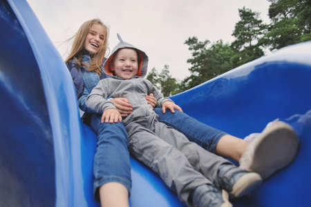 Smiling girl and boy having fun on childrens slideの写真素材