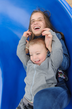 Smiling girl and boy having fun on childrens slideの写真素材
