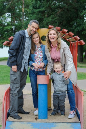 Positive family mother and father with son and daughter playing on playgroundの写真素材