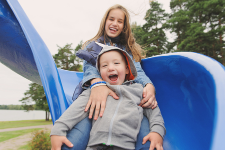 Smiling girl and boy having fun on childrens slideの写真素材