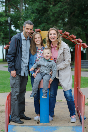 Positive family mother and father with son and daughter playing on playgroundの写真素材