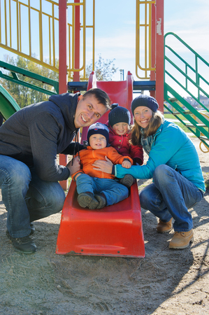 Happy smiling young family of four at childrens playground in parkの写真素材