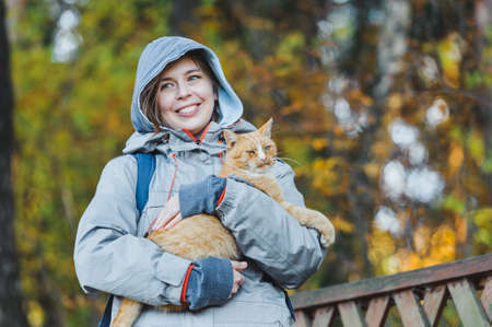 portrait a woman stroking big red fluffy cat on nature. friendship people and animal. smiling woman and her lovely funny pet on walk outdoors. healthy young cat with owner. Pets and lifestyle conceptの写真素材