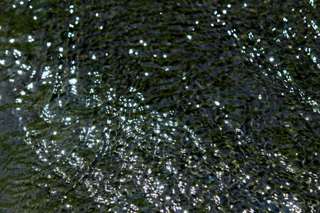 Closeup photo as a background material of pure water flow reflecting glitter and sunlightの写真素材
