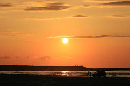 A Japanese couple standing on a sandy beach where the sun sets in the seaの写真素材