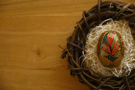 Photo of traditional straw decorated Easter eggs in a bird nest on wooden table with copy space