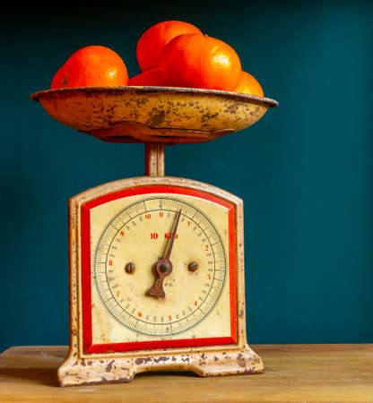 Weighing tangerines in a retro, vintage and worn out scale or balance, on a wooden plank against a guatemala green wall.の写真素材