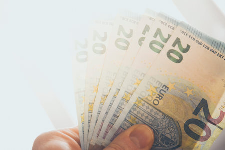 Hand holding spread out 20 euro banknotes against strong sunlight