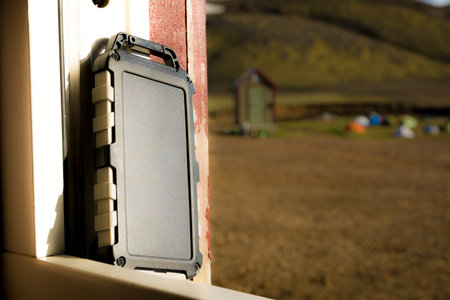 Rugged power bank battery with solar cell charging in the sun, nature and tents of campsite in the backgroundの写真素材