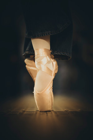 A ballerina feet in pink pointe shoes stand poised on a wooden floor, illuminated in warm light.の写真素材