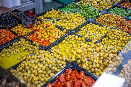 A vibrant market display of various marinated green and yellow olives in trays, seasoned and colorfulの写真素材