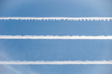 Parallel airplane contrails in a clear blue sky, forming horizontal cloud linesの写真素材